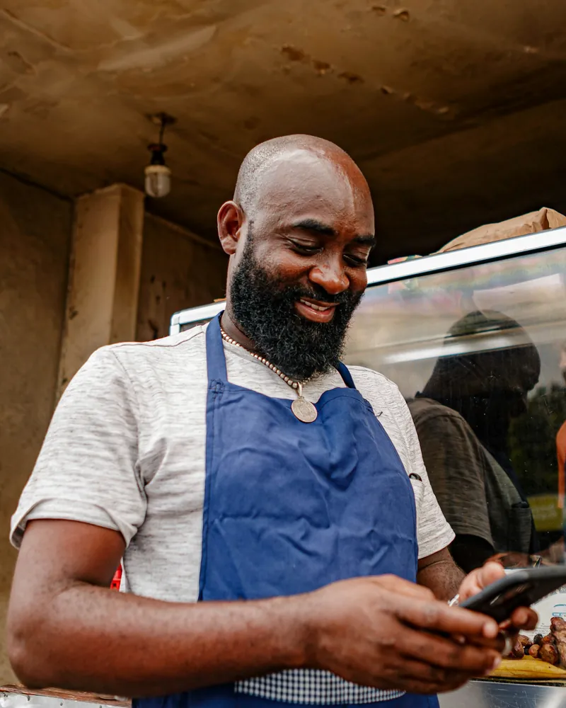 Food vendor in a blue apron smiling at an order on his phone